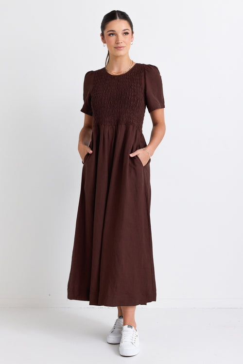 model wears a long brown linen dress with white sneakers