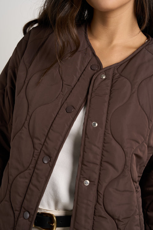 model wears a chocolate brown collarless puffer jacket with  cream jeans