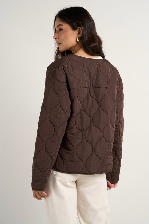 model wears a chocolate brown collarless puffer jacket with  cream jeans