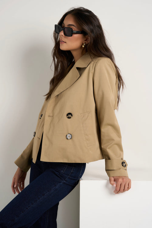 Model wears camel beige trench coat with dark indigo jeans