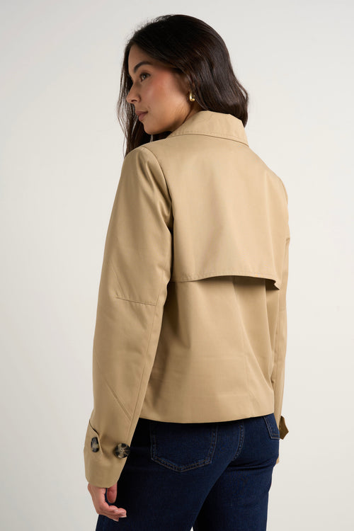 Model wears camel beige trench coat with dark indigo jeans