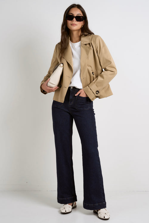 Model wears camel beige trench coat with dark indigo jeans