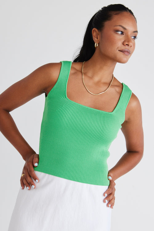 model wears a green top and white linen skirt