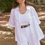 model wears a matching white button up top and shorts set with a white singlet underneath and black glasses