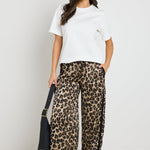 Woman wearing black satin pants with a white side stripe, paired with a white tee for a sporty yet sophisticated look.