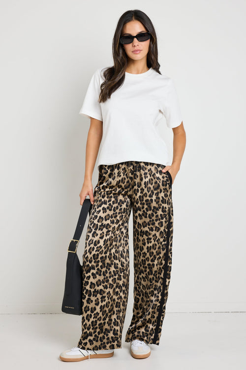 Woman wearing black satin pants with a white side stripe, paired with a white tee for a sporty yet sophisticated look.